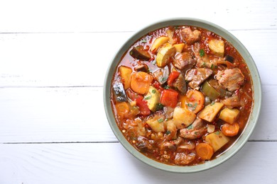 Photo of Delicious stew with vegetables in bowl on white wooden table, top view. Space for text