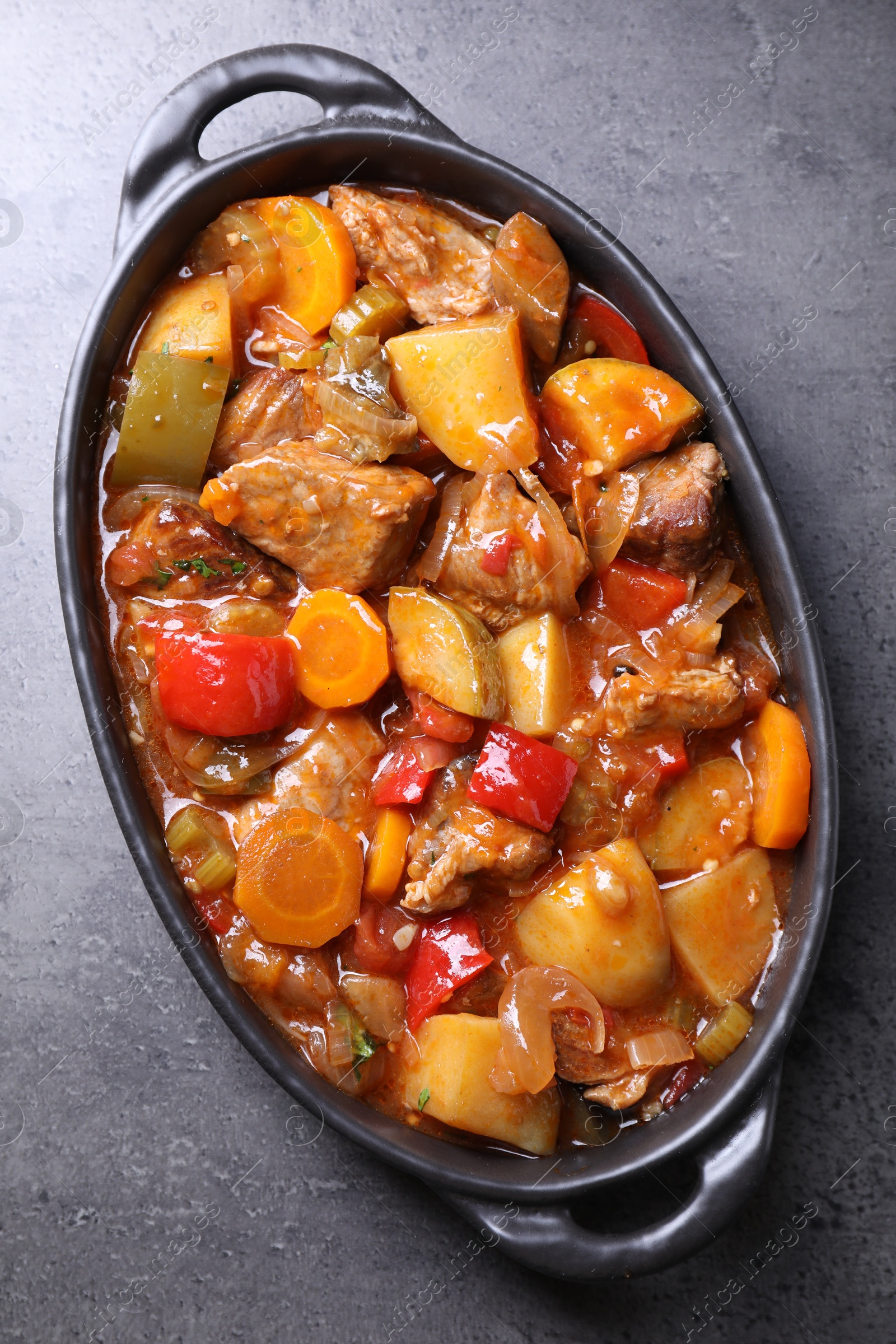 Photo of Delicious stew with vegetables in baking dish on grey table, top view