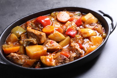 Delicious stew with vegetables in baking dish on grey table, closeup