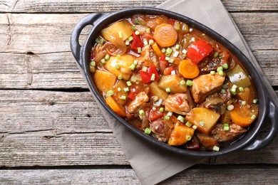 Delicious stew with vegetables in baking dish on wooden table, top view. Space for text