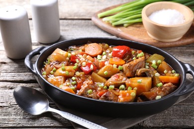 Delicious stew with vegetables in baking dish, spoon and spices on wooden table, closeup