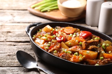 Photo of Delicious stew with vegetables in baking dish and spoon on wooden table, closeup