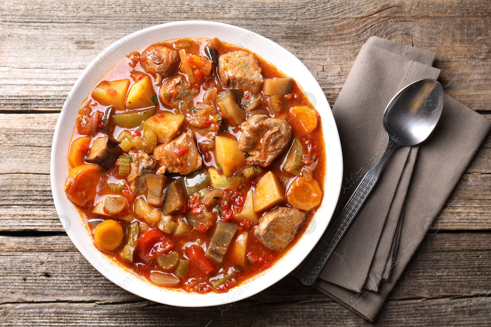 Photo of Delicious stew with vegetables in bowl and spoon on wooden table, top view