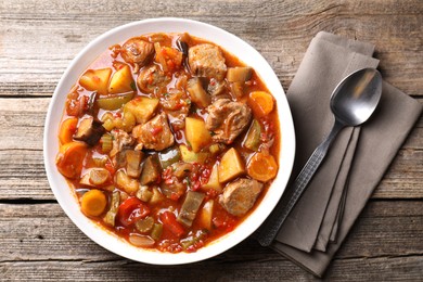 Photo of Delicious stew with vegetables in bowl and spoon on wooden table, top view