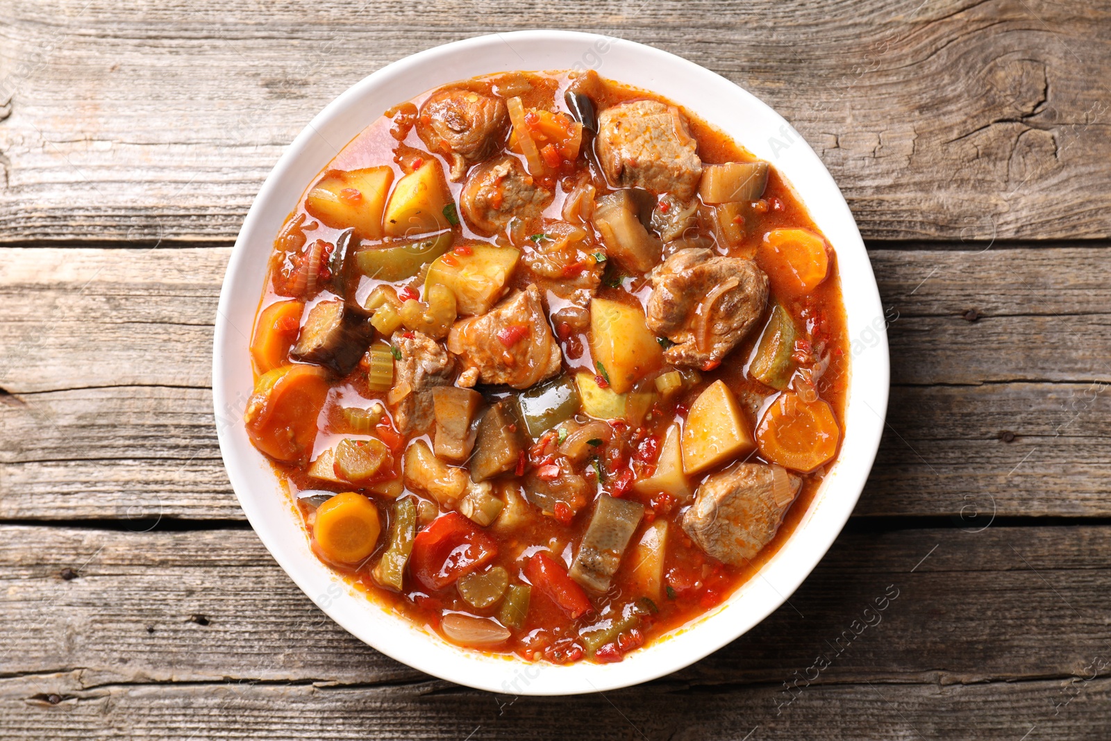 Photo of Delicious stew with vegetables in bowl on wooden table, top view