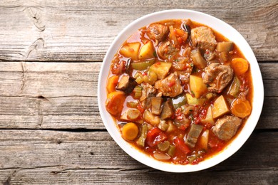 Delicious stew with vegetables in bowl on wooden table, top view. Space for text