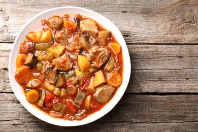 Photo of Delicious stew with vegetables in bowl on wooden table, top view. Space for text