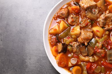 Photo of Delicious stew with vegetables in bowl on grey table, top view. Space for text