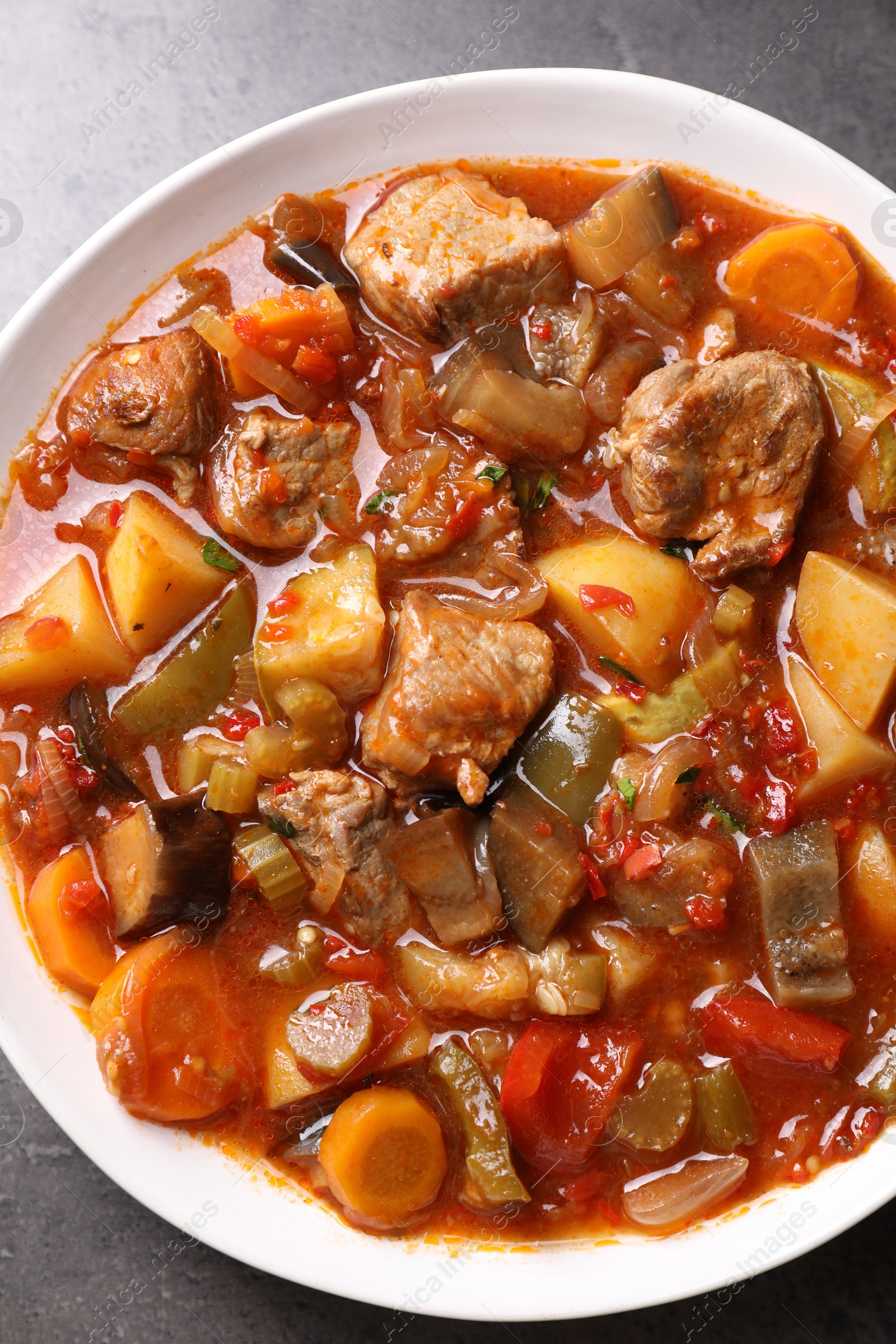 Photo of Delicious stew with vegetables in bowl on grey table, top view