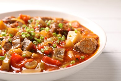 Delicious stew with vegetables in bowl on white wooden table, closeup