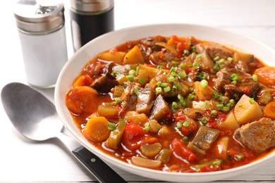 Delicious stew with vegetables in bowl and spoon on table, closeup