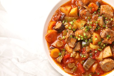 Photo of Delicious stew with vegetables in bowl on white marble table, top view. Space for text