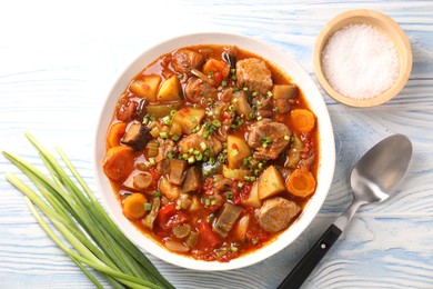 Photo of Delicious stew with vegetables in bowl, spices and spoon on light blue wooden background, top view