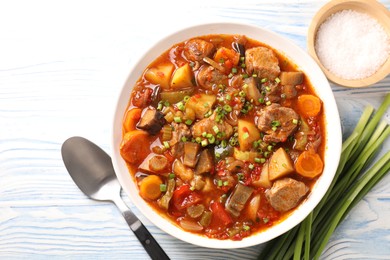 Photo of Delicious stew with vegetables in bowl, spices and spoon on light blue wooden background, top view