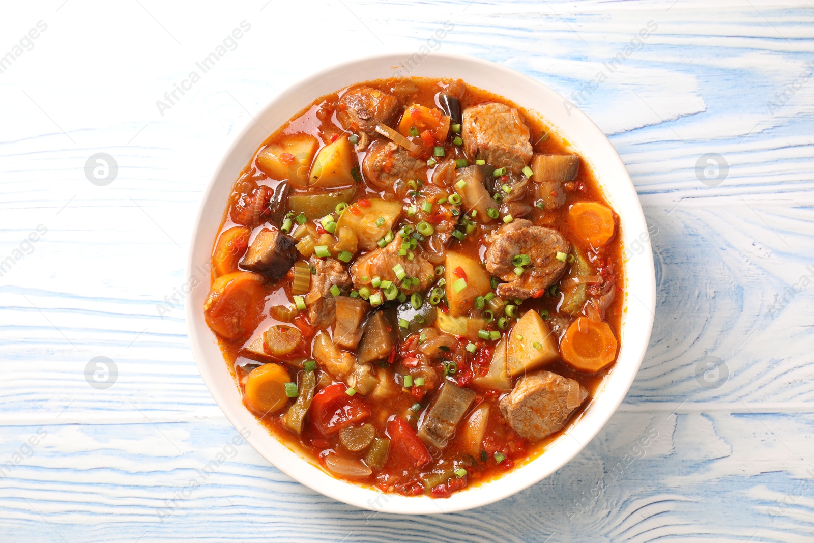 Photo of Delicious stew with vegetables in bowl on light blue wooden background, top view