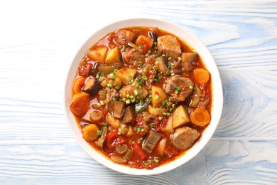 Delicious stew with vegetables in bowl on light blue wooden background, top view