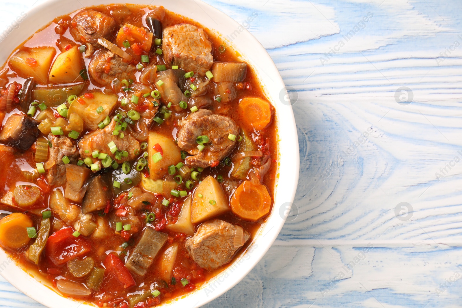 Photo of Delicious stew with vegetables in bowl on light blue wooden background, top view