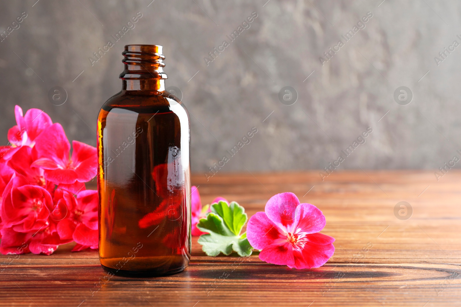 Photo of Geranium essential oil in bottle and beautiful flowers on wooden table