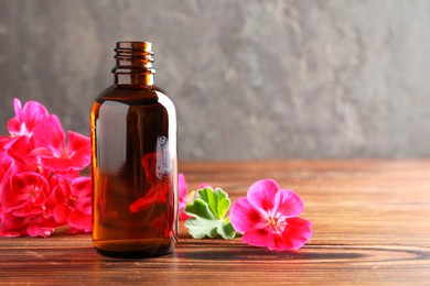 Photo of Geranium essential oil in bottle and beautiful flowers on wooden table