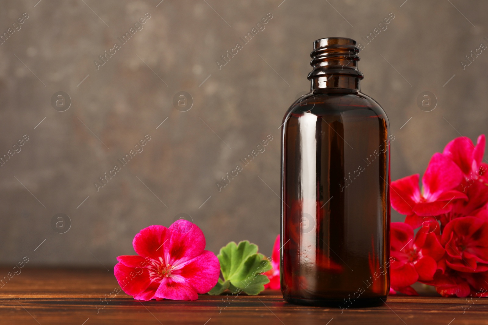 Photo of Geranium essential oil in bottle and beautiful flowers on wooden table