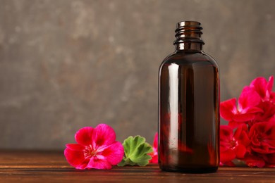 Photo of Geranium essential oil in bottle and beautiful flowers on wooden table