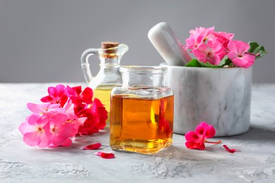 Photo of Geranium essential oil and beautiful flowers on light grey textured table