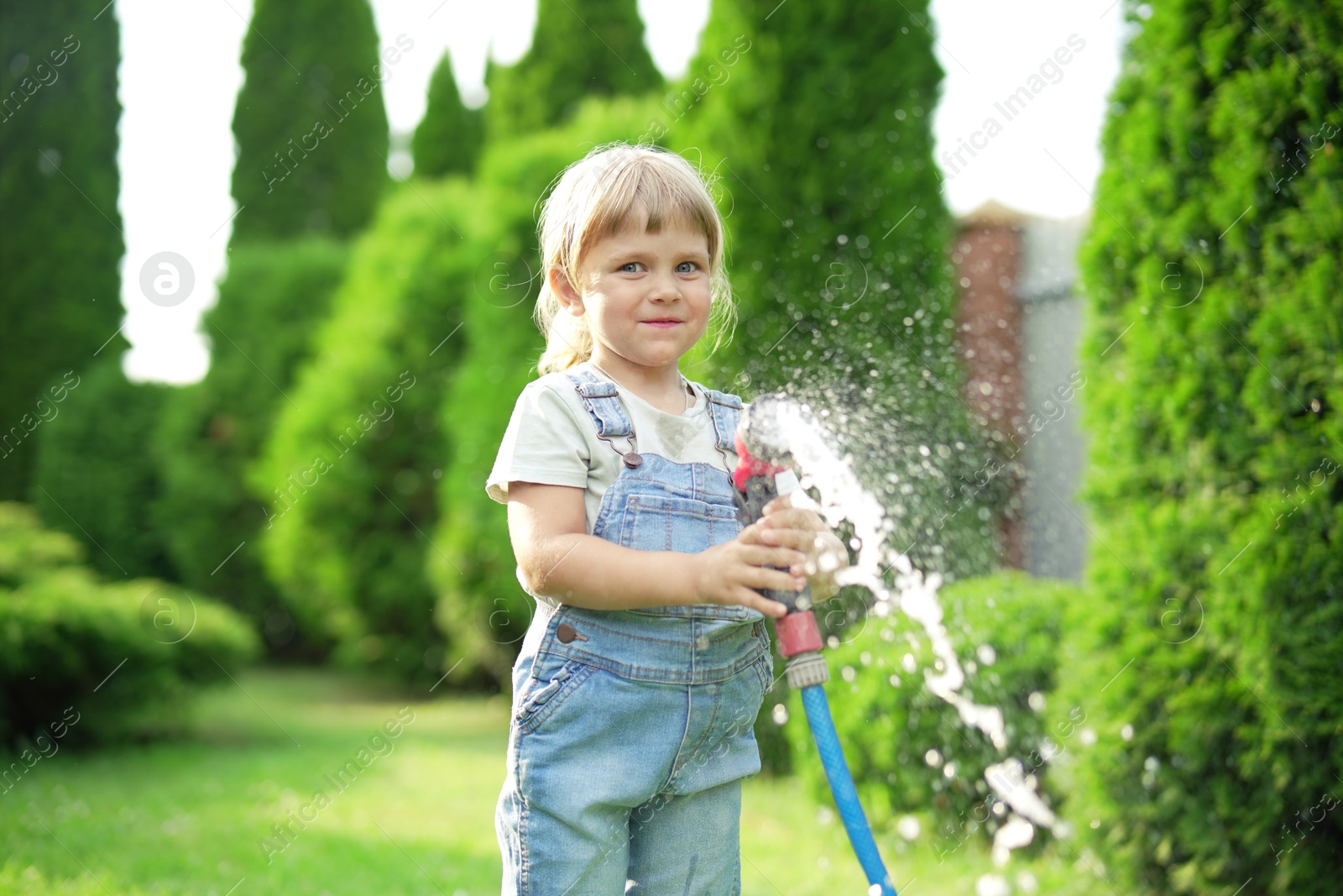 Photo of Little girl watering lawn with hose in backyard