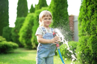 Little girl watering lawn with hose in backyard