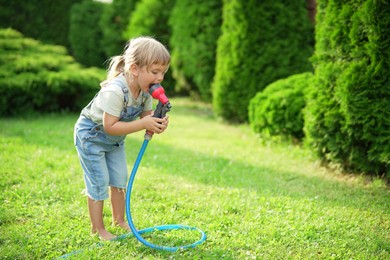 Little girl with hose in backyard, space for text