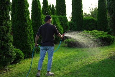 Man watering lawn with hose in backyard