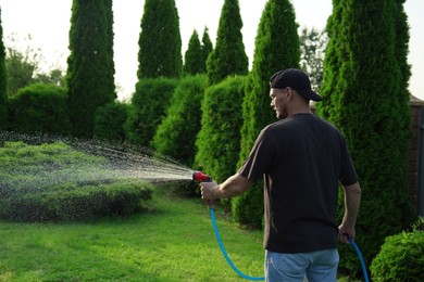 Photo of Man watering lawn with hose in backyard