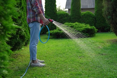 Photo of Man watering green grass on lawn in backyard, closeup