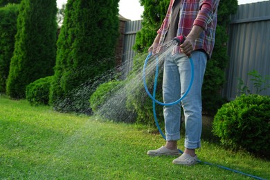 Photo of Man watering green grass on lawn in backyard, closeup