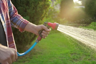 Photo of Man watering lawn with hose in backyard, closeup