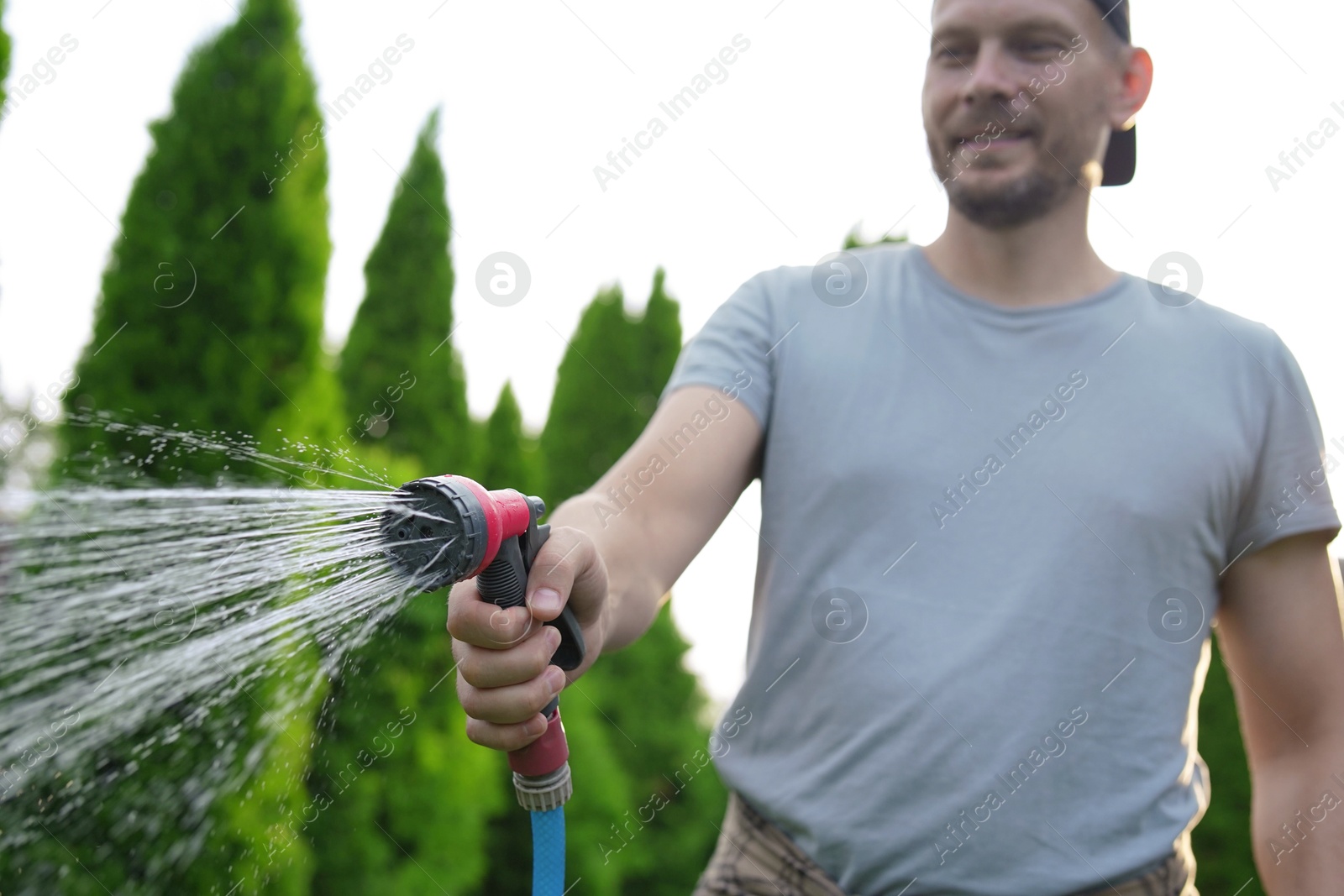 Photo of Man watering lawn with hose in backyard, selective focus