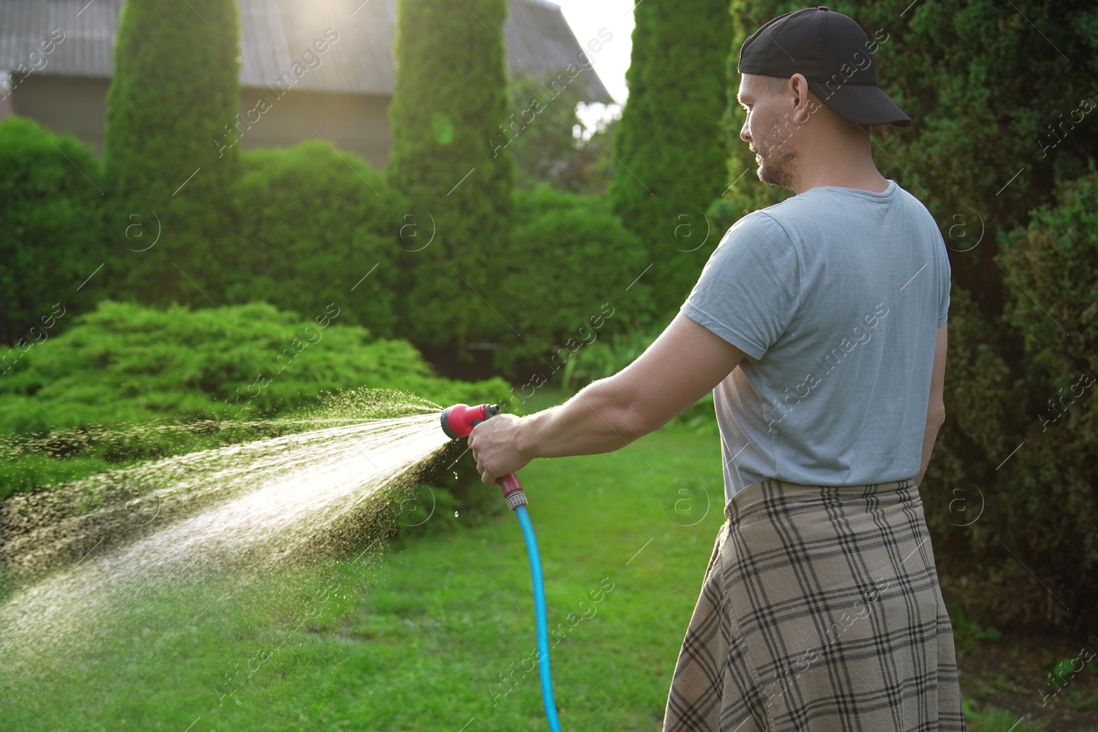 Photo of Man watering lawn with hose in backyard