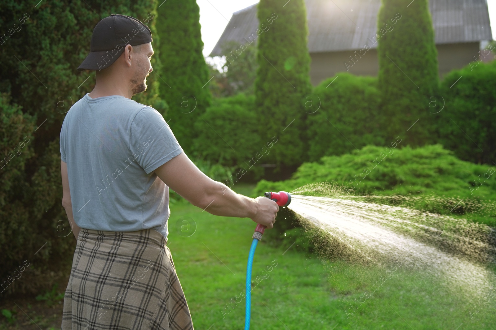 Photo of Man watering lawn with hose in backyard