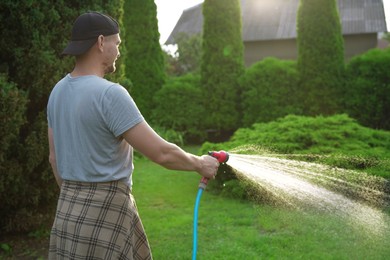 Man watering lawn with hose in backyard