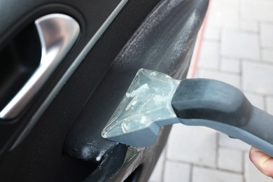 Photo of Man cleaning car door with vacuum cleaner outdoors, closeup