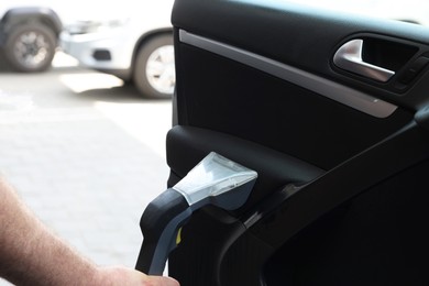 Photo of Man cleaning car door with vacuum cleaner outdoors, closeup