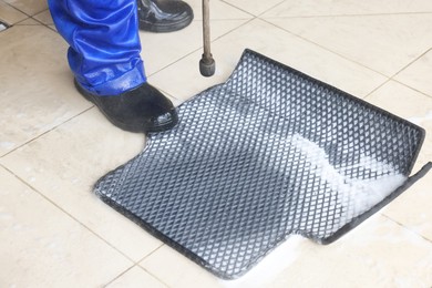 Photo of Man washing rubber car mat with high pressure water jet indoors, closeup