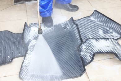 Photo of Man washing rubber car mats with high pressure water jet indoors, closeup