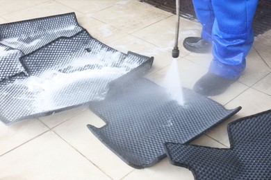 Photo of Man washing rubber car mats with high pressure water jet indoors, closeup