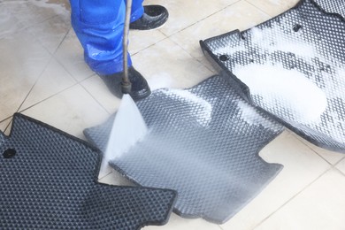 Photo of Man washing rubber car mats with high pressure water jet indoors, closeup