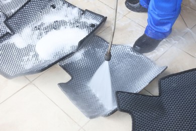 Photo of Man washing rubber car mats with high pressure water jet indoors, closeup