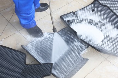 Photo of Man washing rubber car mats with high pressure water jet indoors, closeup