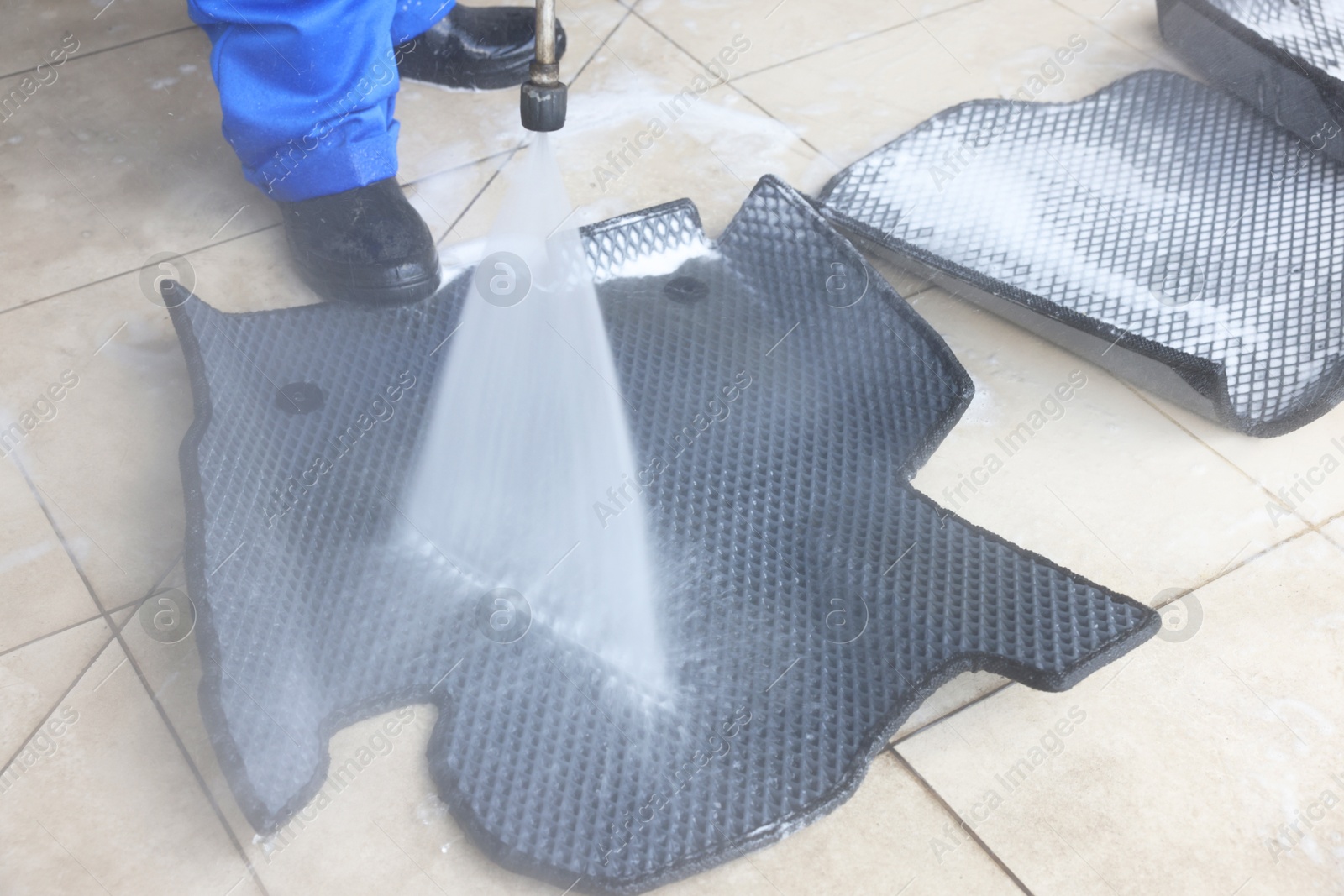 Photo of Man washing rubber car mats with high pressure water jet indoors, closeup