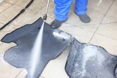 Photo of Man washing rubber car mats with high pressure water jet indoors, closeup