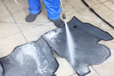 Photo of Man washing rubber car mats with high pressure water jet indoors, closeup