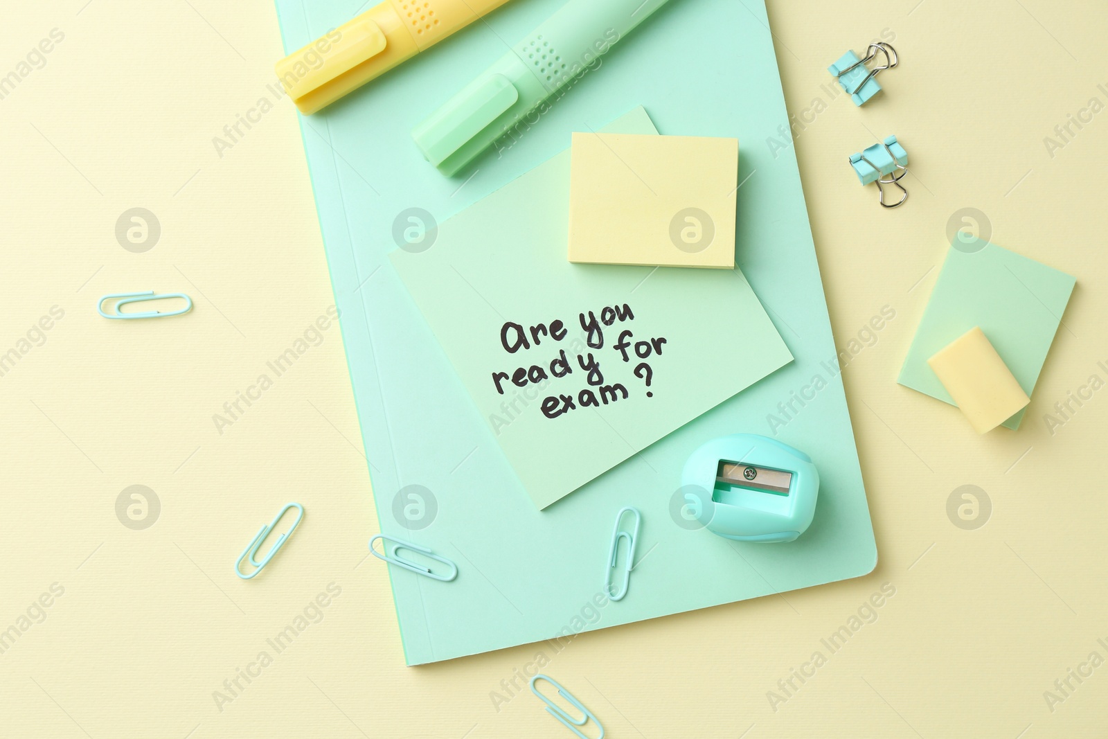 Photo of Paper note with question Are You Ready For Exam and stationery on pale yellow background, flat lay